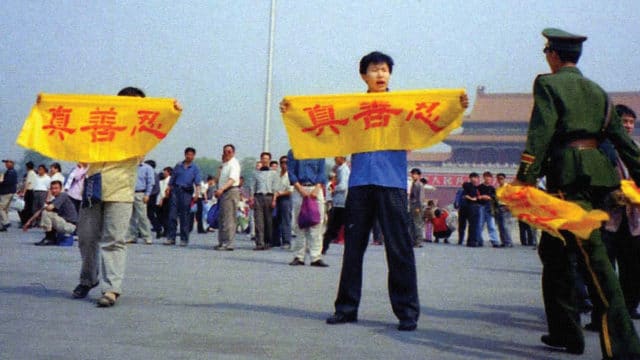 Un poliziotto cinese (a destra) si avvicina ai praticanti del Falun Gong in piazza Tienanmen mentre reggono uno striscione con la scritta “Verità Compassione Tolleranza”.